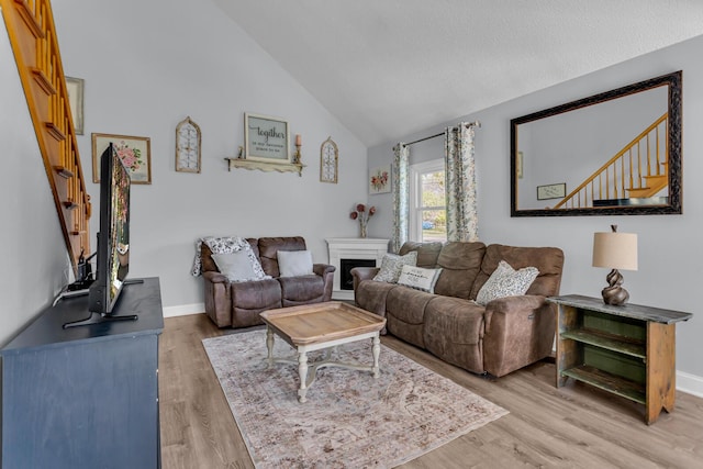 living room featuring light wood-style floors, baseboards, a fireplace, and stairs