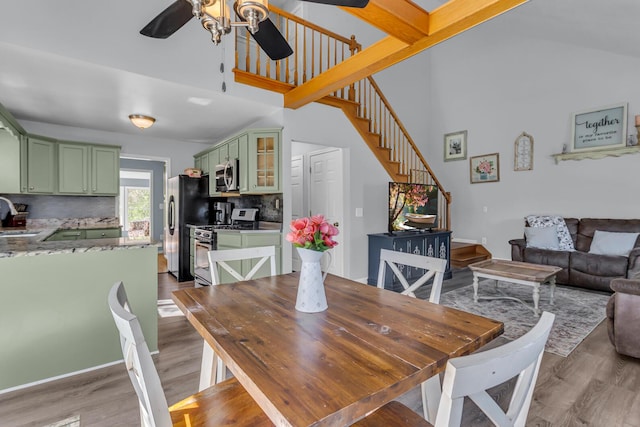 dining space with a towering ceiling, ceiling fan, stairway, and light wood-type flooring