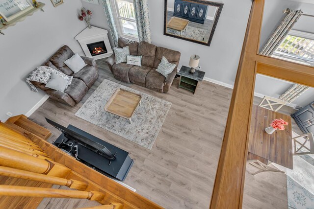living area featuring baseboards, a glass covered fireplace, a wealth of natural light, and wood finished floors
