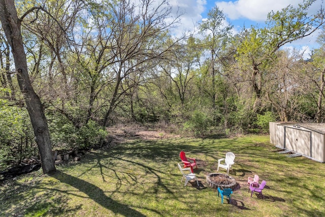 view of yard with an outdoor fire pit, an outbuilding, and a forest view