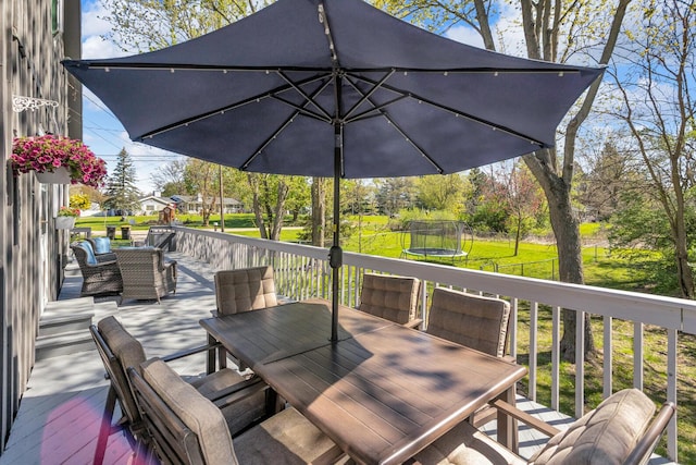 deck with fence, a trampoline, outdoor dining area, and a yard