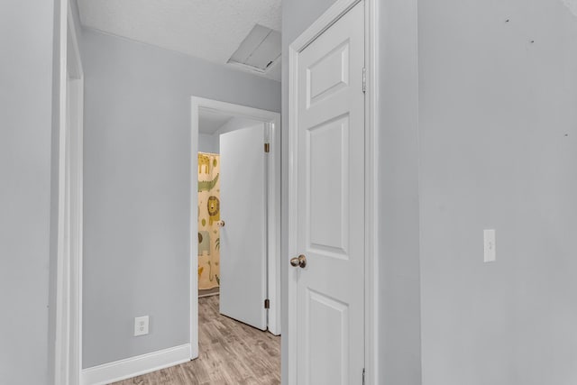 hallway featuring light wood-type flooring, a textured ceiling, and baseboards