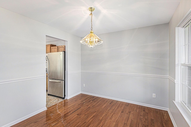 unfurnished dining area featuring baseboards, a notable chandelier, and wood finished floors