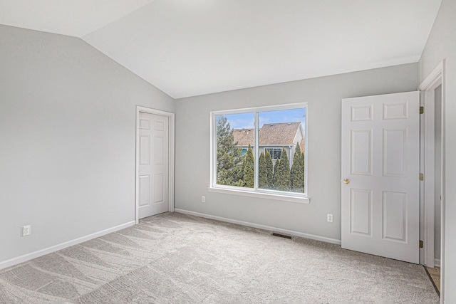 empty room with visible vents, baseboards, vaulted ceiling, and light carpet