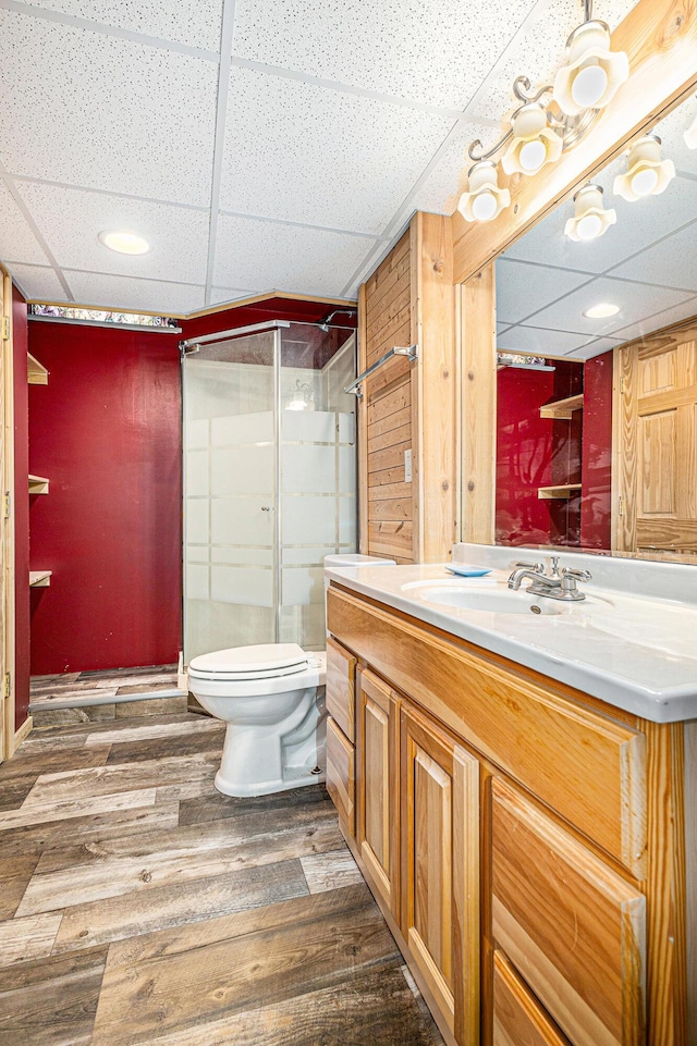bathroom featuring vanity, wood finished floors, toilet, a paneled ceiling, and a stall shower