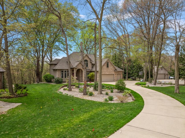 french country home with brick siding, a front lawn, roof with shingles, and concrete driveway
