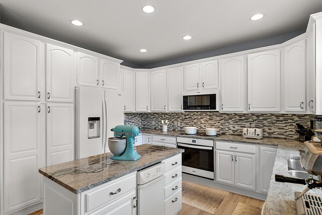 kitchen featuring light stone countertops, stainless steel oven, decorative backsplash, and white refrigerator with ice dispenser