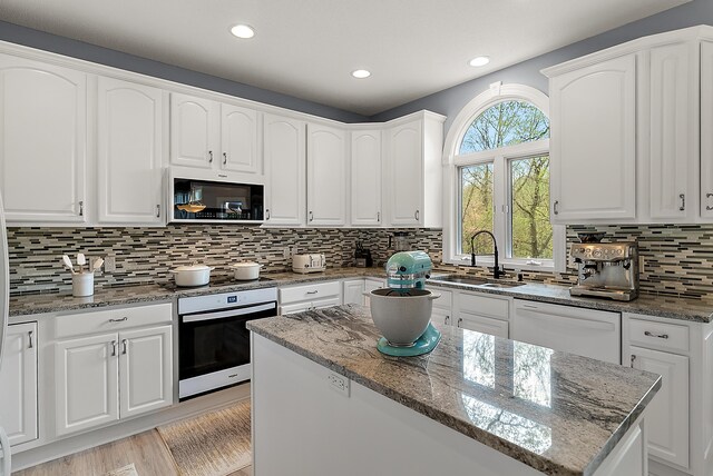 kitchen with stone countertops, wall oven, tasteful backsplash, a sink, and dishwasher