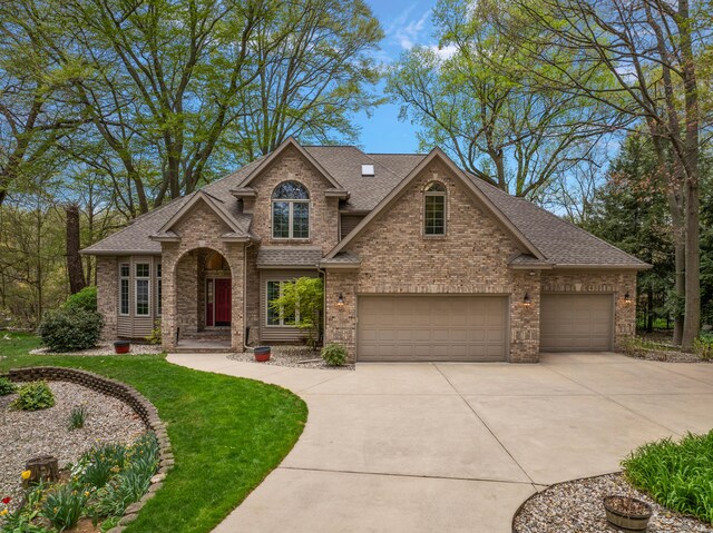 view of front facade featuring roof with shingles, concrete driveway, a front lawn, and brick siding