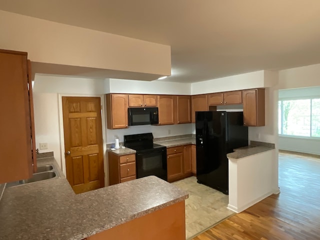 kitchen featuring a peninsula, brown cabinetry, black appliances, and light wood-type flooring