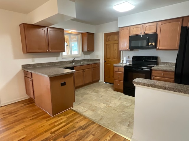 kitchen with a peninsula, dark countertops, a sink, light wood-style flooring, and black appliances