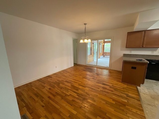 unfurnished dining area featuring baseboards, a notable chandelier, and wood finished floors