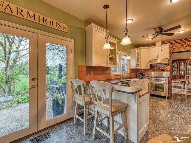 6603 S Stony Creek Rd, Monroe, MI 48162 - kitchen with high end stainless steel range oven, dark countertops, hanging light fixtures, a peninsula, and under cabinet range hood