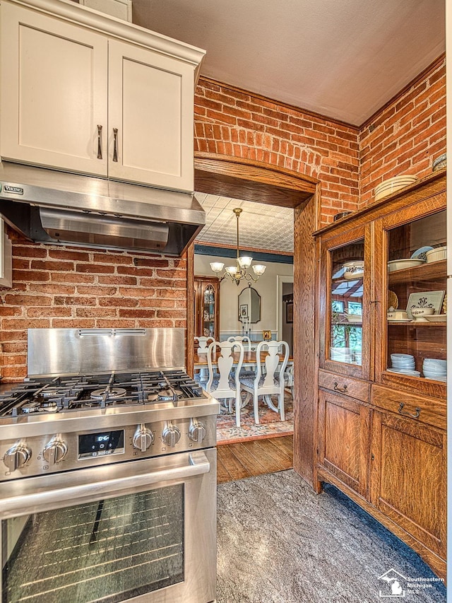 6603 S Stony Creek Rd, Monroe, MI 48162 - kitchen featuring stainless steel range with gas stovetop, a notable chandelier, brick wall, and under cabinet range hood