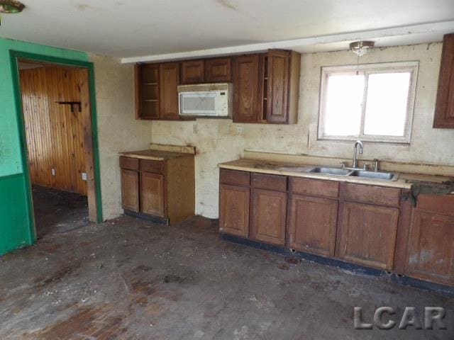 kitchen with brown cabinetry, a sink, and white microwave