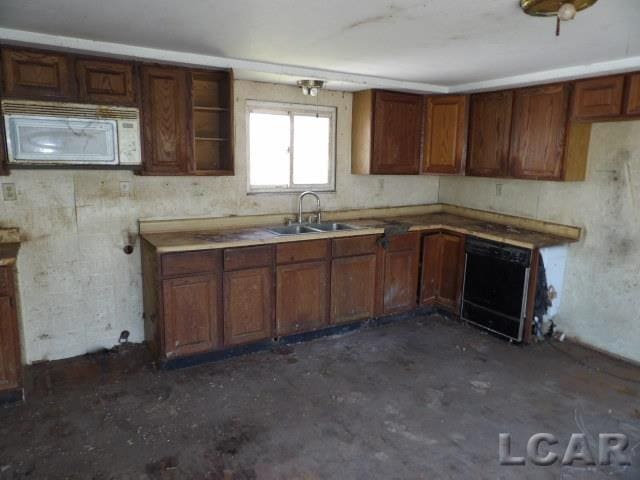 kitchen with brown cabinetry, a sink, white microwave, concrete floors, and black dishwasher