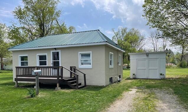 back of house with a storage unit, stucco siding, a yard, and a deck