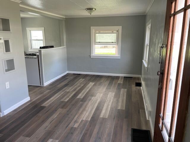 spare room featuring baseboards, ornamental molding, dark wood-type flooring, and visible vents