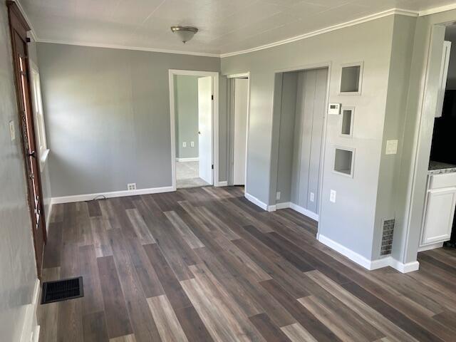 empty room featuring baseboards, ornamental molding, dark wood-style floors, and visible vents