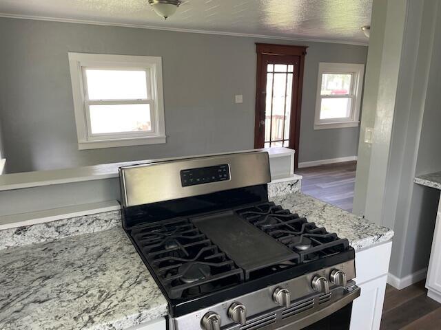 kitchen with crown molding, stainless steel range with gas stovetop, baseboards, and dark wood-style floors