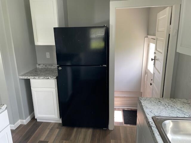 kitchen with freestanding refrigerator, dark wood-style flooring, light stone countertops, baseboards, and white cabinets