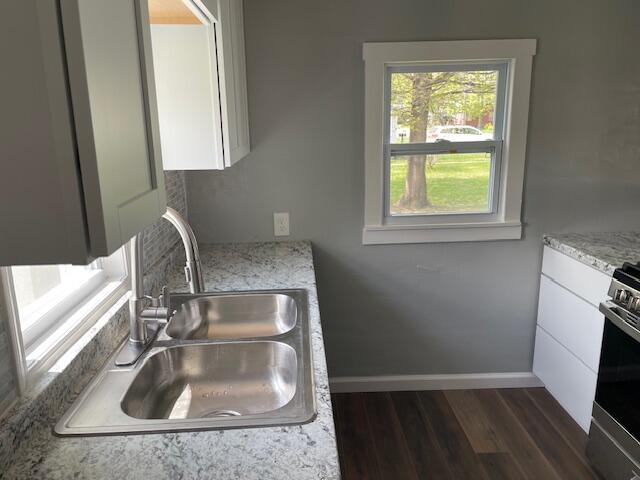 kitchen featuring a sink, stainless steel range with gas cooktop, white cabinetry, and dark wood-type flooring