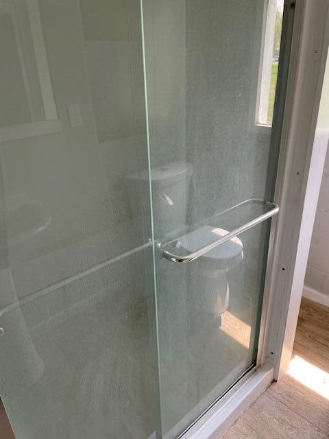 bathroom with toilet, wood finished floors, and a stall shower