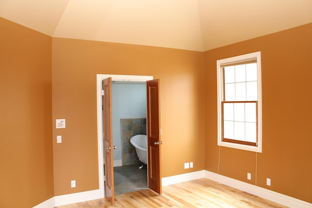 unfurnished bedroom with baseboards, vaulted ceiling, and light wood-type flooring