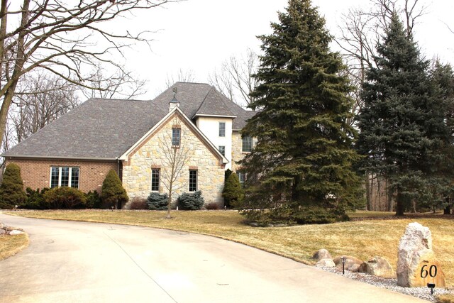 french country style house with driveway, stone siding, and a front lawn