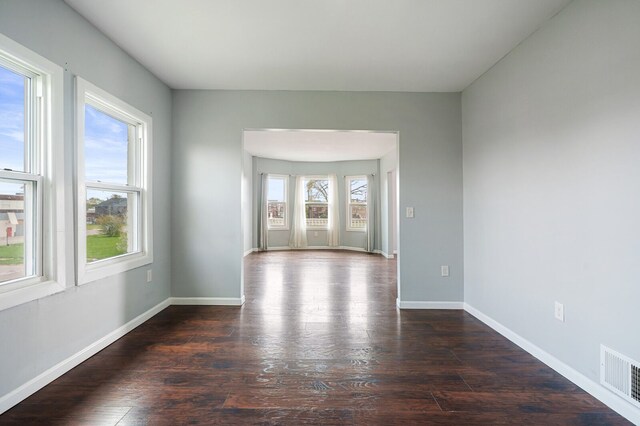 unfurnished room featuring baseboards, visible vents, and dark wood finished floors
