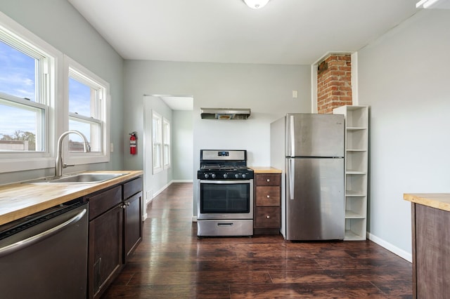 kitchen featuring dark brown cabinetry, a sink, dark wood-style floors, wood counters, and stainless steel appliances
