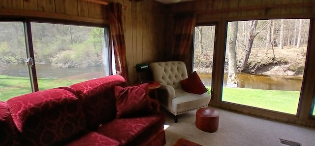 sunroom with visible vents, wood walls, carpet, and a water view
