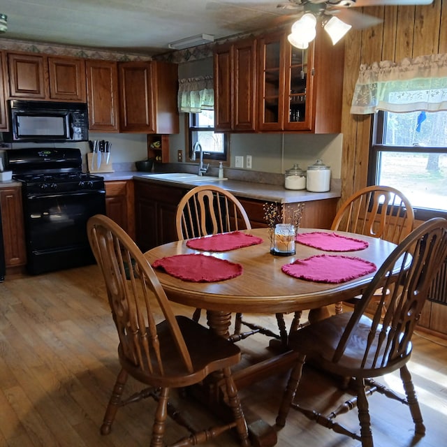 kitchen with light wood-style floors, brown cabinetry, a ceiling fan, and black appliances