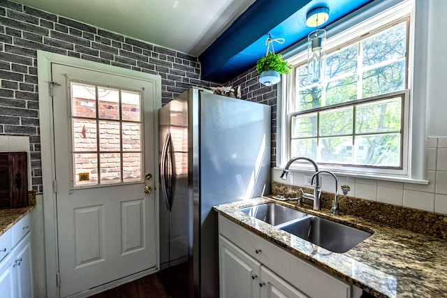 kitchen featuring freestanding refrigerator, a sink, plenty of natural light, and stone countertops