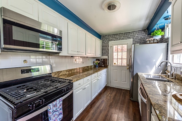 kitchen with appliances with stainless steel finishes, a sink, dark wood finished floors, white cabinets, and dark stone counters