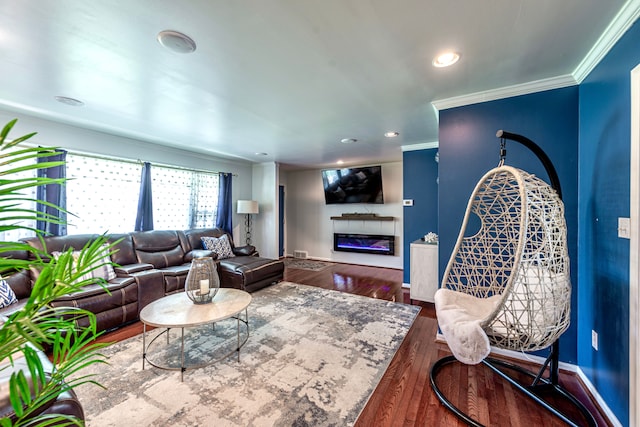 living area with a glass covered fireplace, ornamental molding, baseboards, wood finished floors, and recessed lighting
