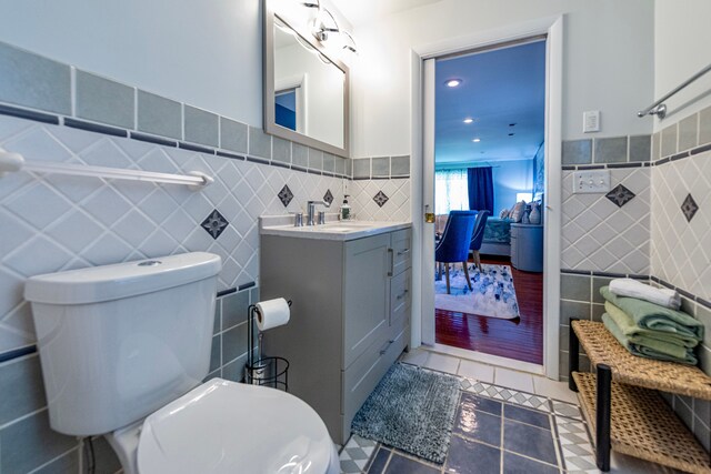 full bathroom featuring tile walls, tile patterned flooring, toilet, vanity, and a wainscoted wall