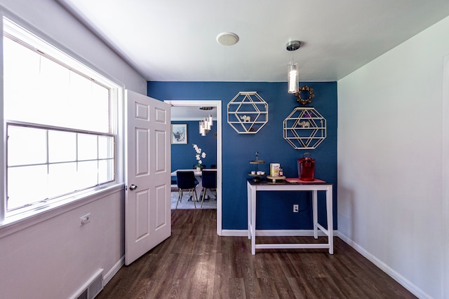 hallway with dark wood-type flooring, baseboards, and a chandelier