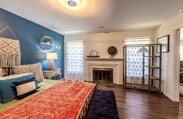 bedroom with wood finished floors, a glass covered fireplace, and baseboards