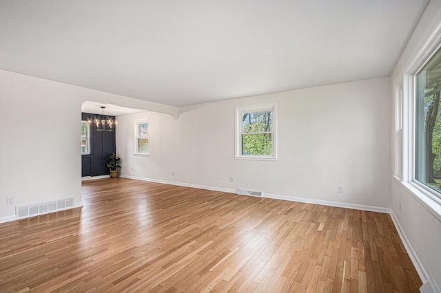 unfurnished room with a healthy amount of sunlight, visible vents, light wood finished floors, and a chandelier
