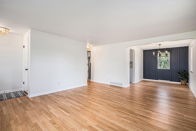 unfurnished living room featuring arched walkways, light wood finished floors, a chandelier, and visible vents