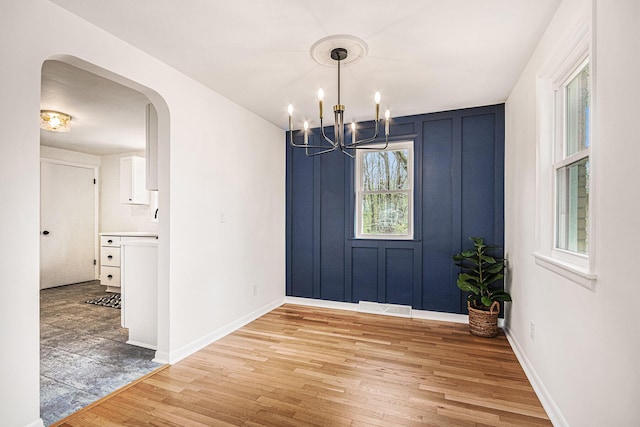 unfurnished dining area with a notable chandelier, arched walkways, light wood-style flooring, baseboards, and visible vents