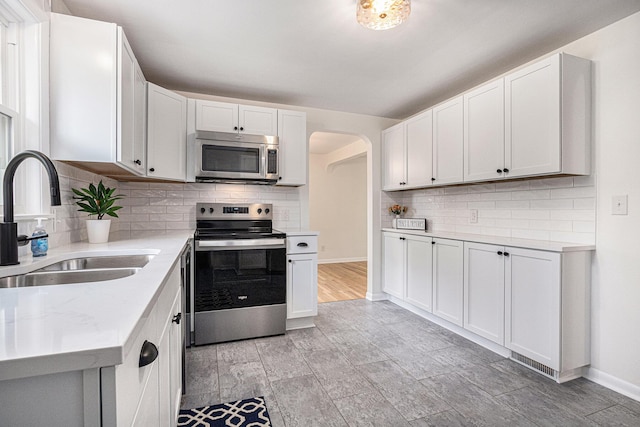 kitchen featuring appliances with stainless steel finishes, a sink, arched walkways, white cabinetry, and decorative backsplash