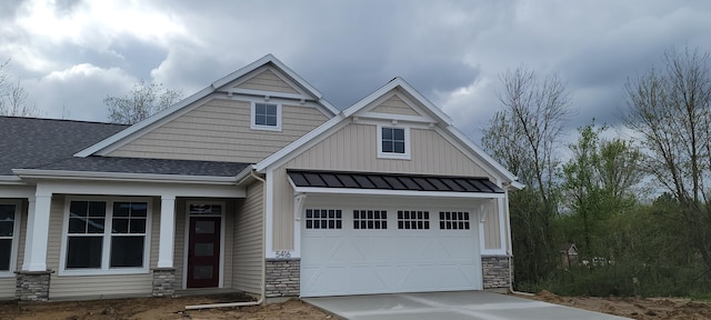craftsman-style house with a standing seam roof, roof with shingles, driveway, and stone siding