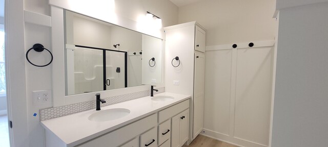 bathroom featuring double vanity, a shower stall, a sink, and wood finished floors