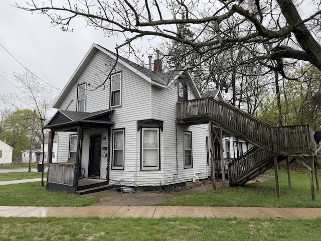 view of front facade with roof with shingles, a deck, a chimney, and a front lawn