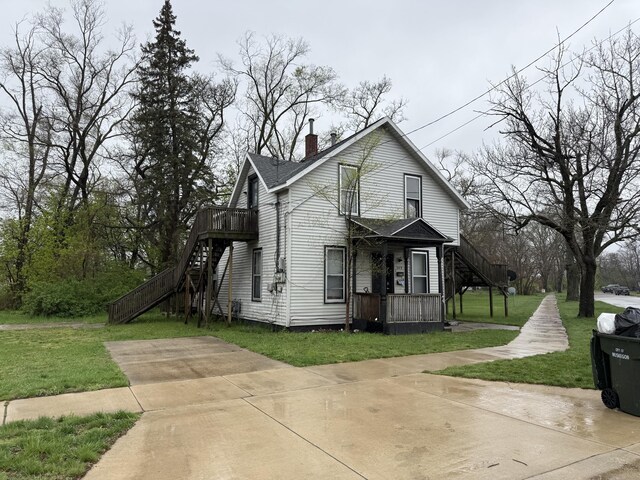 view of front of house featuring a wooden deck, a chimney, stairway, and a front yard