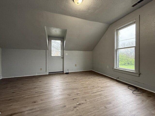 additional living space with vaulted ceiling, a healthy amount of sunlight, visible vents, and wood finished floors