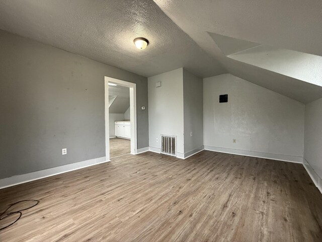 additional living space with a textured ceiling, visible vents, vaulted ceiling, wood finished floors, and baseboards