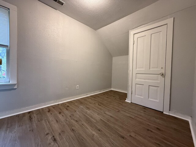 bonus room with a textured ceiling, baseboards, vaulted ceiling, and dark wood-style floors